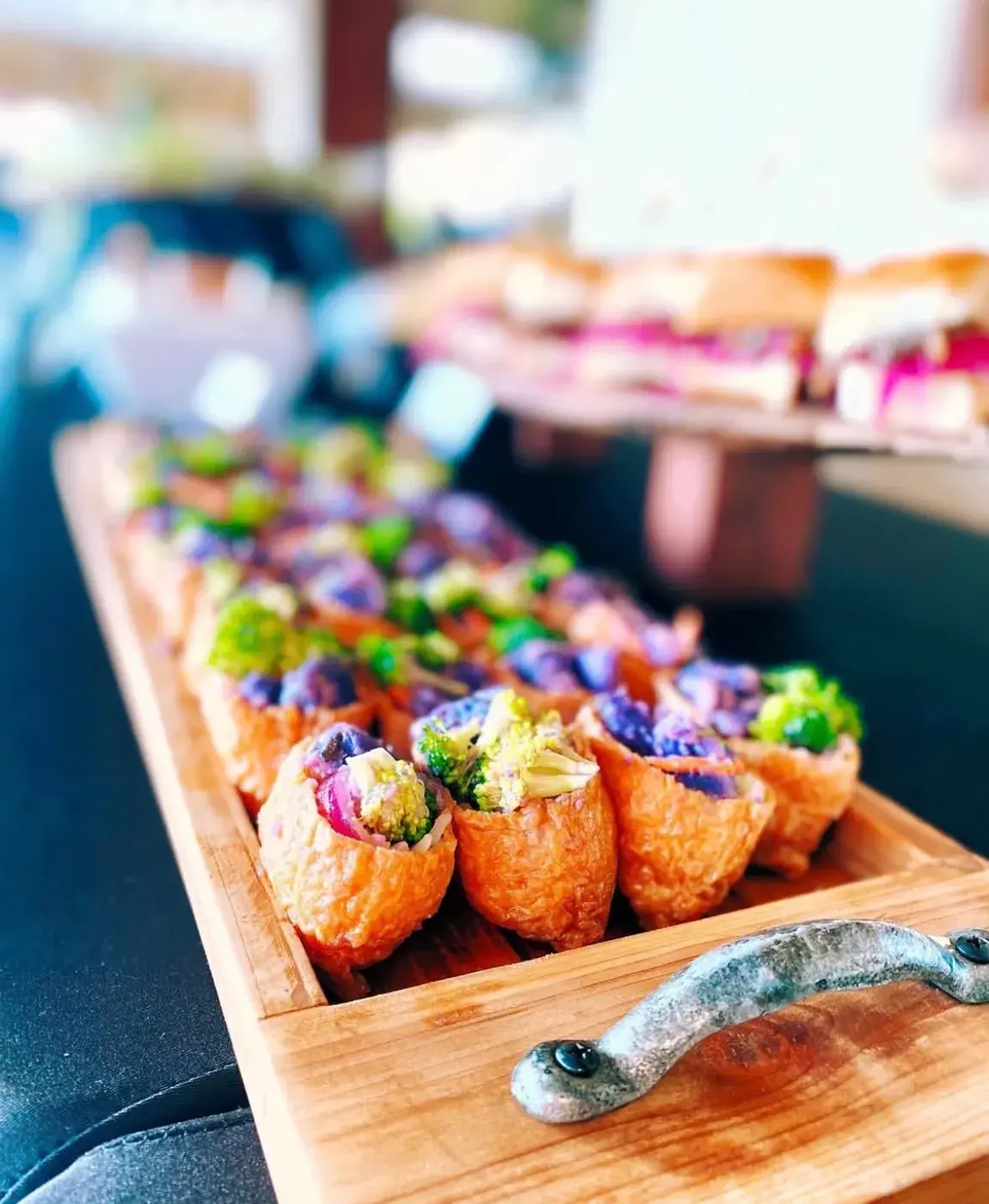 Bite-size pupus topped with edible flowers on a long wooden board