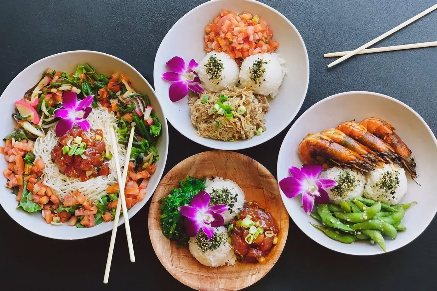 Four Umekes bowls of ahi poke, kalua pork, and garlic shrimp with orchids and rice