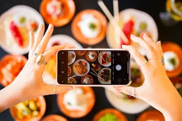 Hands taking a phone photo of a table full of Umekes poke and Hawaiian dishes