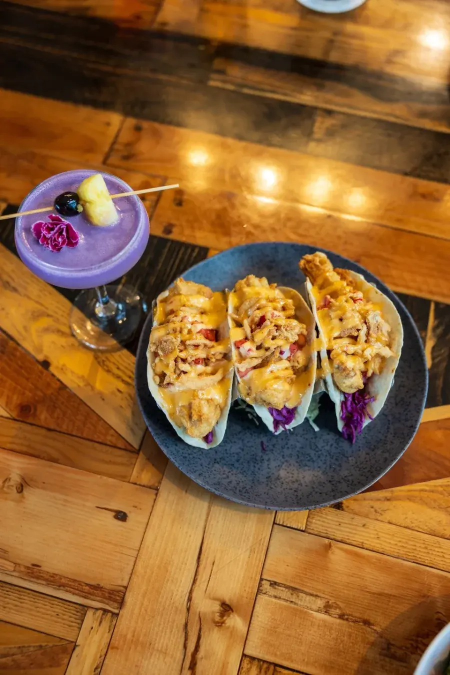 Umekes fish tacos on a stone plate beside a lilikoi cocktail