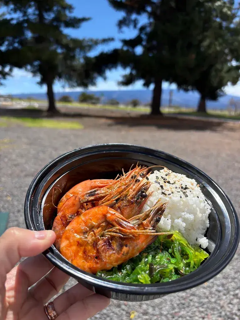 A garlic shrimp bowl with rice and greens from Umekes Saddle Stop, held up outside